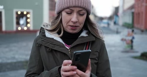 Portrait of Mature Woman in Wool Hat Standing on the Urban Street with Mobile Phone in Hand