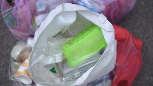 Mano delgada de mujer que coloca un vaso de plástico usado vacío en una bolsa de basura dejando un primer plano
