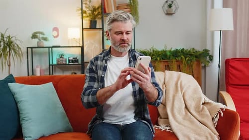 Mature Man Uses Smartphone on Sofa