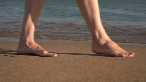 A Woman Walks on the Wet Sea Sand Along the Beach Legs Closeup