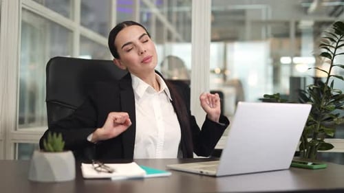 Female Manager Sitting at Office Desk and Stretching While Using Laptop in Room