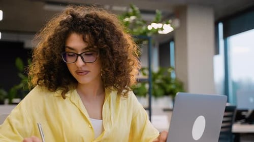 Smiling Woman Taking Notes at Her Desk