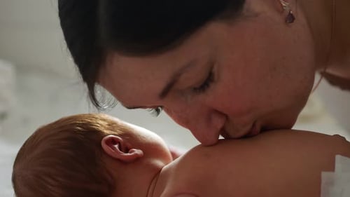 Loving Mother Affectionately Kissing Newborn Baby Indoors