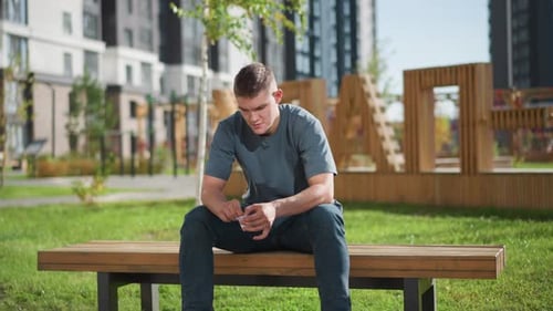 Young Man Opens Packet on Bench in Urban Park