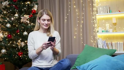 Woman Celebrates Using Phone Next to Christmas Tree