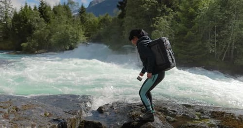 Female Traveler with a Backpack Drinking Water in Nature in the Forest Near a Mountain River