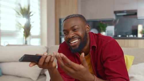 Man Laughing and Changing Channels on Sofa