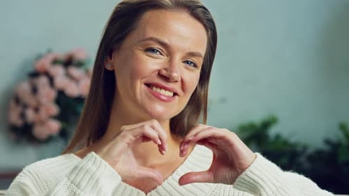 Woman Makes Heart Gesture Toward Camera Indoors
