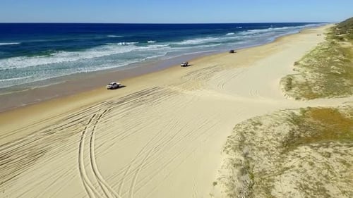 Smooth, sweeping shot of cars, four-wheel driving on the beaches of the iconic Fraser Island on a be