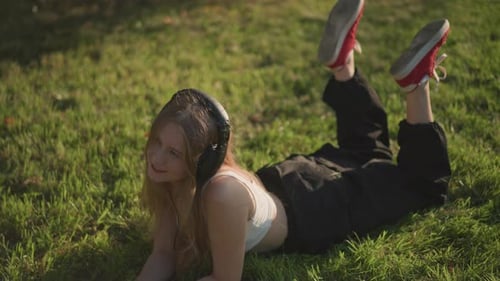 Blonde Woman Listening to Headphones Lying on Grass