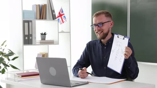 Englischlehrer gibt Online-Unterricht per Laptop am weißen Schreibtisch im Klassenzimmer