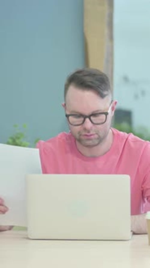 Man Reviews Documents at Desk with Laptop
