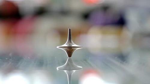 Silver Spinning Top Rotation on Reflective Surface