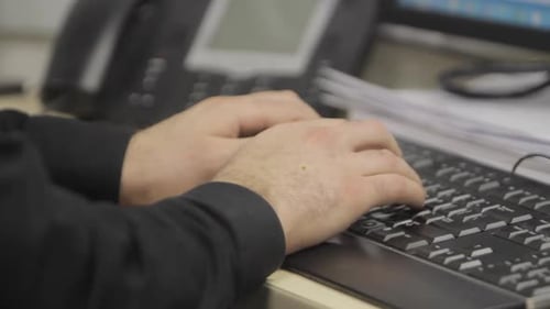 Close up of mans wearing a black shirt hands typing on a desktop keyboard in office.
