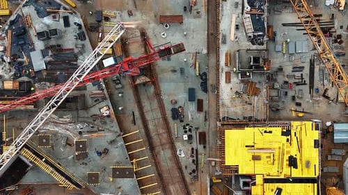 A busy construction site with cranes and building materials during the day, aerial view