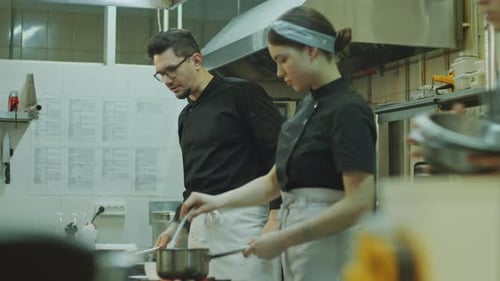 Chef cocinando con la ayuda de una aprendiz en la cocina del restaurante