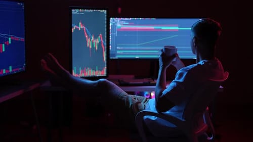 Young Stock Market Trader Analyzing Realtime Charts on Multiple Computer Monitors in Dimly Lit Room