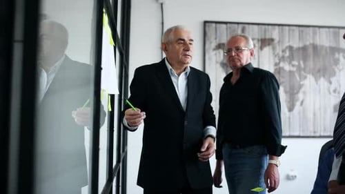 Aged team of elderly businessman architects in the office near glass with plan talking