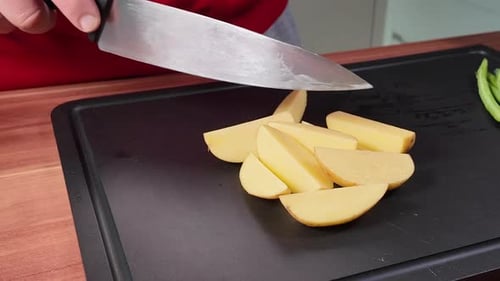 Foto em close-up de mãos cortando uma batata fresca em pedaços iguais em uma tábua de cortar com uma ponta afiada