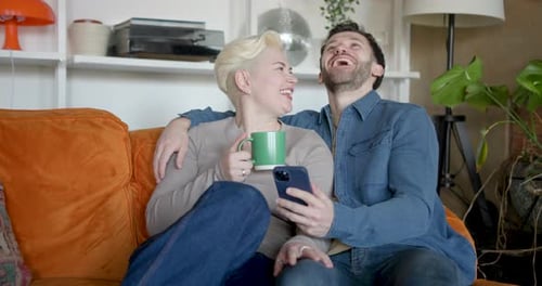 Smiling Couple Relaxing on Couch with Mobile Phone