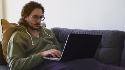 Young Adult Types on Laptop on Couch Indoors