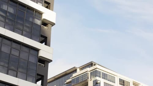 La cámara se inclina hacia arriba y revela una fachada de gran altura que pasa por los balcones contra un cielo azul pálido
