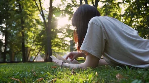 Una joven atractiva acostada en la hierba verde y leyendo un libro