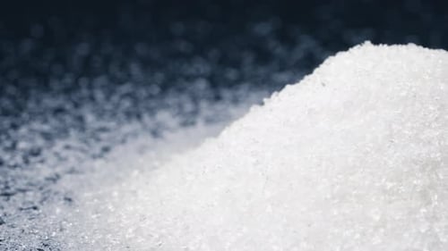Nahaufnahme auf schwarzem und blauem Hintergrund liegt auf weißen, krümeligen granulierten Zuckerkristallen darüber. Gießen Sie auf eine