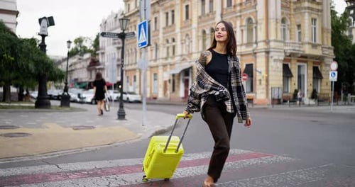 A Happy Brunette Girl in a Checkered Shirt and with a Tattoo Crosses the Road at a Pedestrian
