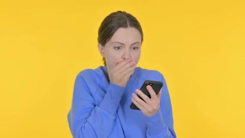 Shocked Woman Looking at Phone on Yellow Background