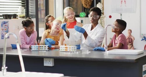 Diverse female teacher and happy schoolchildren having science class in school lab
