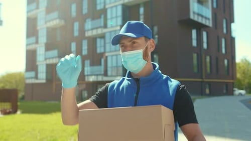 At Sunlight Delivery Man Holding Cardboard Box at Street Wear Protective Medical Face Mask and