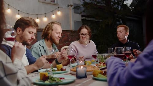 Friends Gather Around Dinner Table Outdoors At Night