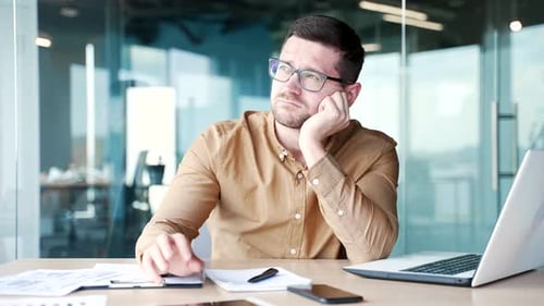 Overworked young worker is bored while sitting at desk at workplace in business office. Sleepy