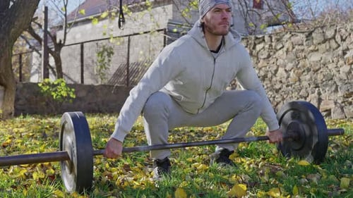 Handsome Muscular Man Doing Exercise with Barbell at Outdoor Gym in Autumn Park