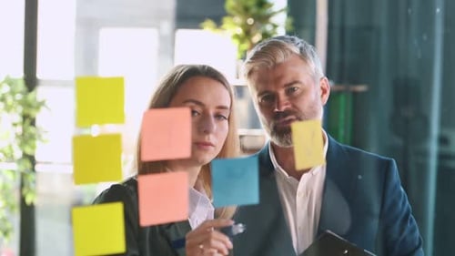 Businessman with woman is working in the office. Standing near glass with stickers. Ideas and plans