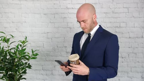 Ein Geschäftsmann schaut auf sein Handy. Der Mann surft auf seinem Handy mit einem Kaffee in seinem anderen