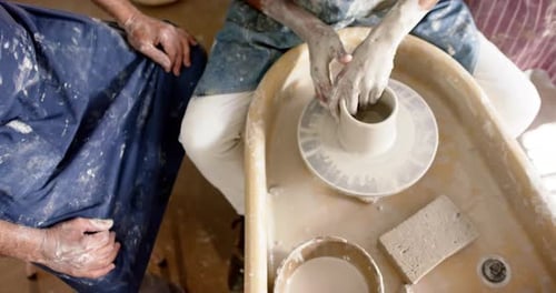 Hands of diverse male potters using potter's wheel in pottery studio, slow motion