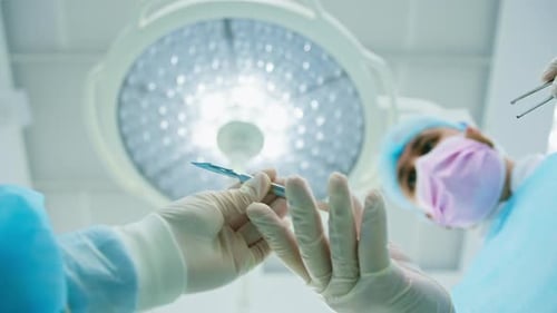 Surgeon Holding Scalpel Under Surgical Lamp