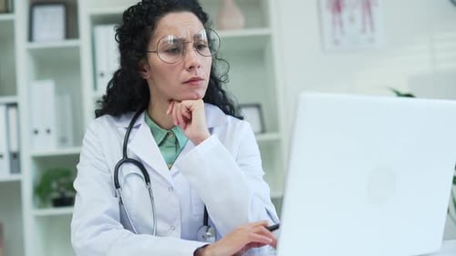 Close up. A serious female doctor is using, typing on a laptop while sitting at a desk at a workplac