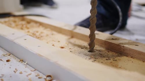 Employee Drills Hole in Wooden Part with Instrument on Floor
