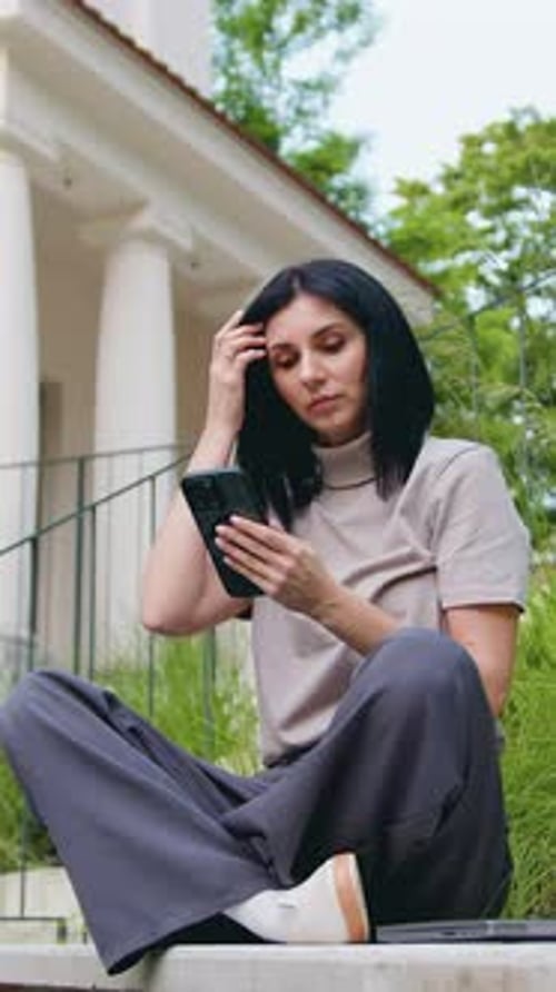 Young Lady in Casual Clothes Focused on Her Phone with a Subtle Smile Residential Building in the