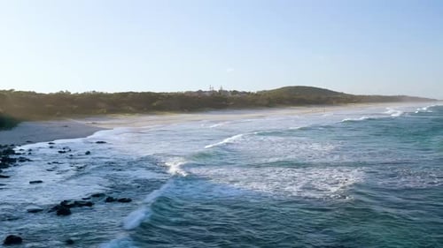 serene beach with soft waves gently hitting the rocky shoreline. The coastline extends into the dist