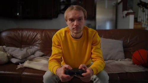 Front View Portrait of Blond Adult Man Sitting on Couch Playing Video Game with Joystick Medium Shot