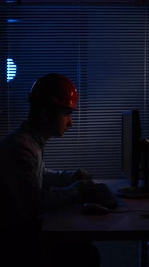 Man wearing hard hat working late at computer