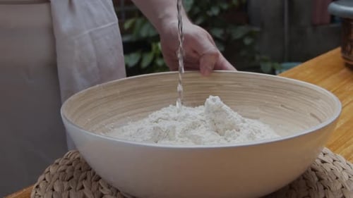 Der Koch gießt Wasser auf den Pizzateig in einem tiefen Teller. Rezept für die Zubereitung von Pizza. Zeitlupe.
