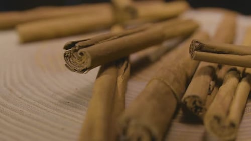 Ceylon cinnamon sticks falling into frame on wooden platform. Close up. slow motion.