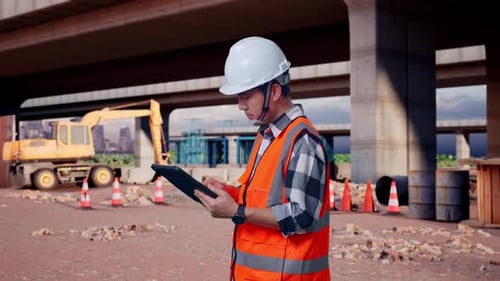 Side View Of Asian Male Engineer Looking At The Tablet In His Hand At Building Site