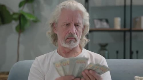 Senior Man Counting Money Indoors with Frustration