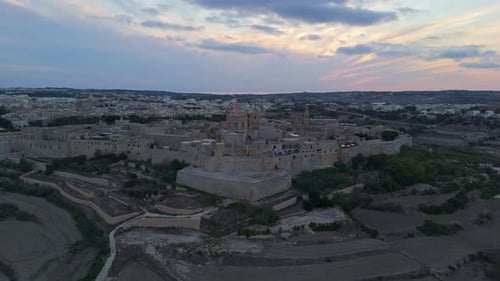 Aerial view of Mdina, Malta, showcasing medieval architecture and countryside at sunset.